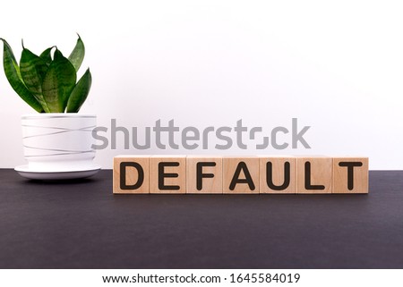 DEFAULT word concept on wooden blocks on a black table with a green flower on a white background. Unemployment