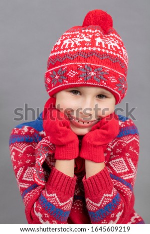 Joyful child in winter clothes on a gray background. Boy in a red knitted hat. Fashionable boy in the studio on a gray background.