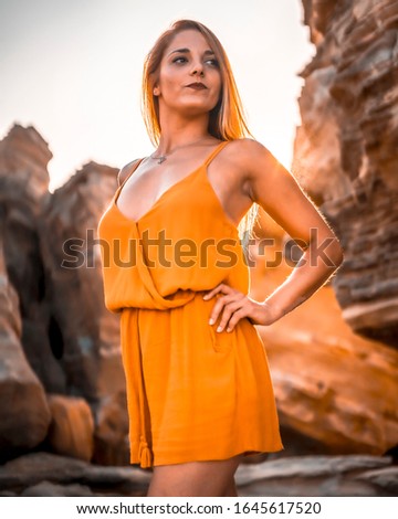 Lifestyle portrait, young serious blonde in an orange dress on some rocks