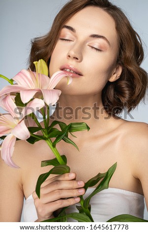 So tender. Pleased female person keeping eyes closed, posing on camera with lilies