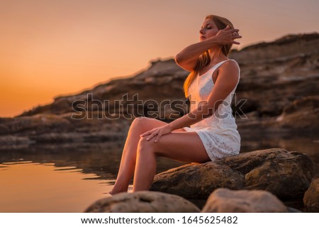 Lifestyle, a young blonde sitting in the water in a white dress on the coast of Basque Country
