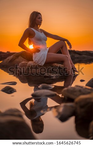 Lifestyle, a young blonde reflected in the water some rocks with a white dress on the coast of Basque Country