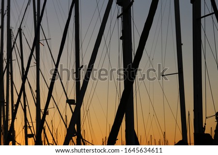 Close up outdoor view of pattern of tall boat masts in a Mediterranean marina, France. Abstract sunset picture with geometric shapes and many crossed lines. Orange blue sky in background.