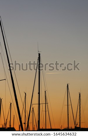 Close up outdoor view of pattern of tall boat masts in a Mediterranean marina, France. Abstract sunset picture with geometric shapes and many crossed lines. Orange blue sky in background.