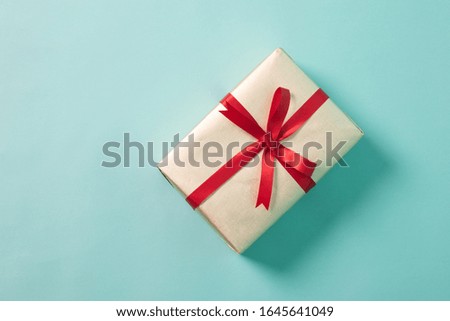 Golden gift box with red ribbon on cyan background