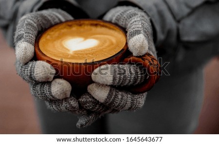 female hands in gloves hold a cup of hot cappuccino coffee on the street