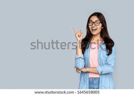 Amazed young happy indian girl student lady shopper professional excited face looking at camera pointing finger at copy space surprised by shopping sale offer isolated on gray studio background. Royalty-Free Stock Photo #1645658005