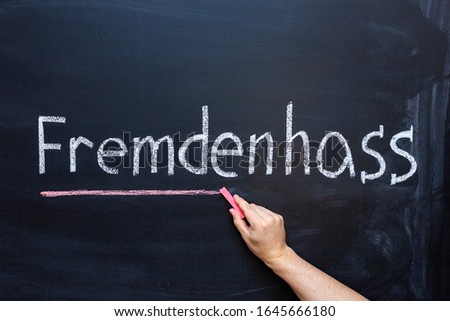 The man emphasizes the word xenophobia with red chalk. The word xenophobia in the German language on the chalk Board.