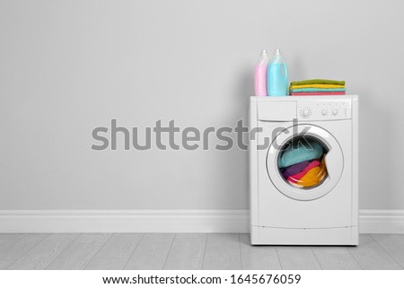 Modern washing machine with stack of towels and detergents near white wall, space for text. Laundry day
