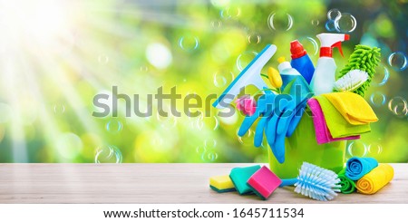 Bucket with cleaning items on blurry spring background with sun beams and soapbubbles