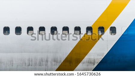 Dirty aircraft body with windows. Yellow and blue lines. Airplane details. Royalty-Free Stock Photo #1645730626