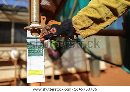 Site scaffolder supervisor hand wearing safety CS5 glove protection inspecting scaffolding tag label on standing tube ensure its safe up to date prior used  on construction site    