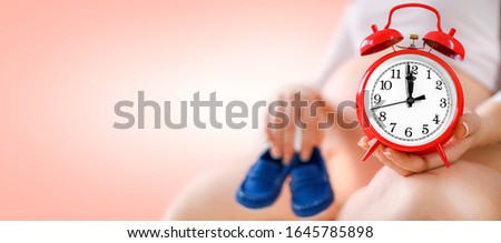 Detail photo of pregnant woman in background with red alarm clock near tummy or baby belly. Maternity time comming banner. Copy space for text.