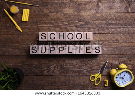 Word school supplies in wooden cubes, blocks on the subject of education, development and training on a wooden background. Top view. Place for text