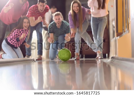 Young woman throwing ball and spending time with friends in bowling club