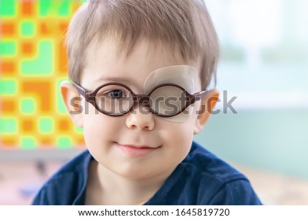 A little boy wearing glasses and an eye patch (plaster, occluder) undergoes a hardware vision treatment to prevent amblyopia and strabismus (squint, lazy eye). Child congenital vision disease problem Royalty-Free Stock Photo #1645819720