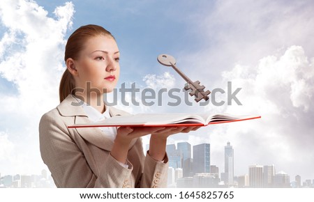 Woman looks at flying big metal key above open book. Real estate agency advertising. Sale of commercial or private real property concept. Elegant girl with book on background of business center.