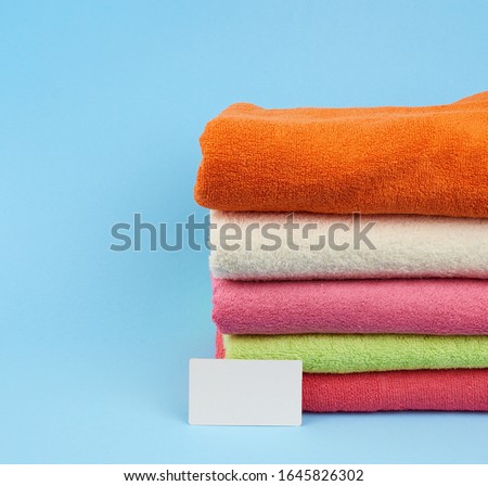 stack of multi-colored terry towels to wipe the body after a shower and a white blank paper business card on a blue background