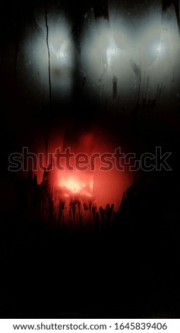 Misted glass window with red and grey lights in night darkness. Blurry abstract background with copy space. Defocused reflection in glass surface. Colorful blur on black backdrop.