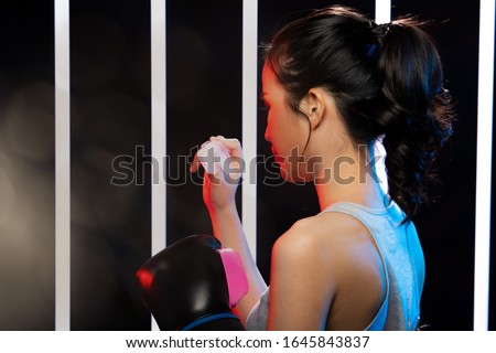 Beautiful Asian Woman is training and holding boxing mouth guards with Black Pink Mitts Gloves in hand. Office Girl exercises in Modern Fashion Neon Muay Thai Boxer Gym, copy space