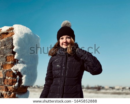 a portrait of a teenage girl in winter clothes on sky background next to brick wall
