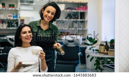 My favorite specialist. Close up photo of attractive woman with beautiful makeup drinking coffee and looking in the mirror while talking with a hairstylist.