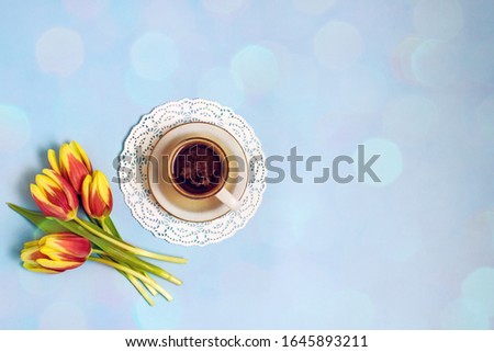 Cup of coffee and tulips on a blue background. A bouquet of five red tulips next to coffee. Coffee and flowers background. The concept of good morning, mother's day, women's day, birthday. Flat lay