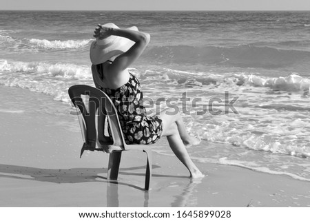 Black and white photograph. Girl sitting on a broken chair. Woman in hat on the beach funny photo. broken chair on the beach.