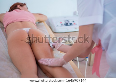 Unrecognizable fat woman lies on a sofa with a stomach and receives an electric thigh massage. Vacuum slimming procedure.