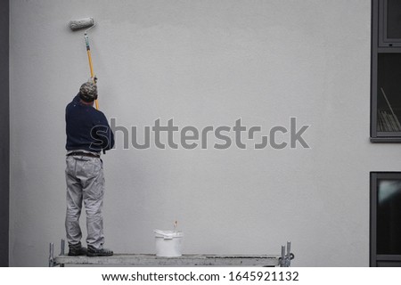 a male painter paints the wall with a roller blue paint. outdoor work in an apartment building and multi-storey building. Royalty-Free Stock Photo #1645921132