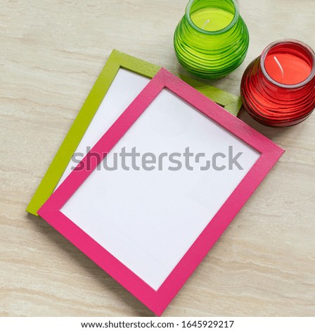 On the table are green and pink photo frames, green and red candles