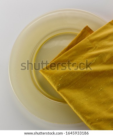 Yellow silk napkin on a yellow glass plate. Close-up on white background