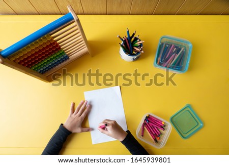 a child draws on the yellow table. Top view