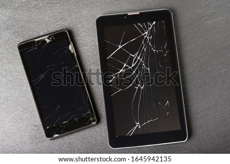 A phone and a tablet computer with broken screens lie on a stone. View from above. Close-up