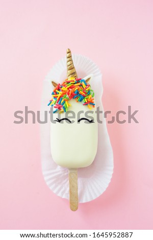 Unicorn popsicle with closed eyes on a pink background. Glazed with white chocolate.
