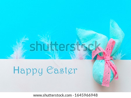 Egg gift in green paper packaging and with pink ribbon Easter Bunny wrap idea.  multicolor colorful feathers. Minimal concept. Flat lay, Copy space, top view