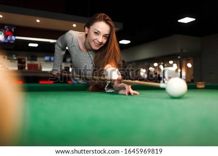 Young smiling woman plays billiards in a pub