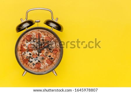 Black alarm clock with a pizza instead of a dial. Yellow background.