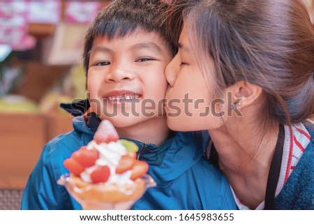 Mother is kissing her son smiling while eating strawberry dessert ice cream in japanese cafe.