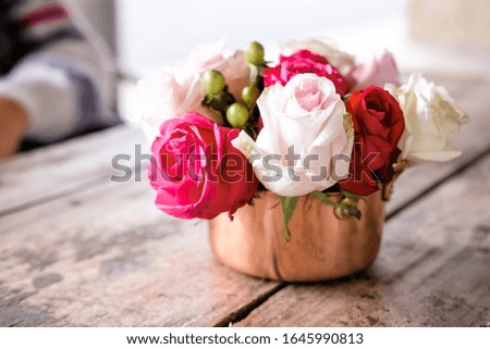 Pink and white roses in copper dish on textured wooden table in outdoor cafe. Lifestyle concept. 