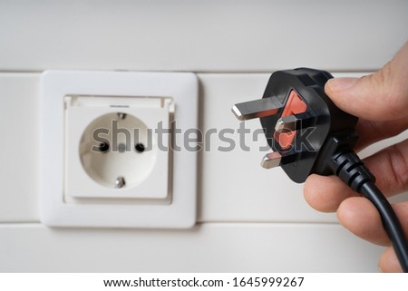 Hand Holding Incompatible AC Plug Near Wall Socket Royalty-Free Stock Photo #1645999267