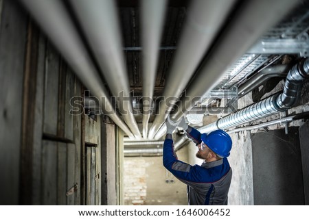 Male Worker Inspecting Water Pipes For Leaks In Basement Royalty-Free Stock Photo #1646006452