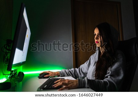 Young girl sitting in the dark infront of computer screen with green light in the back