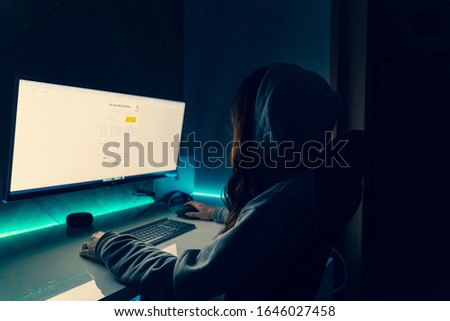 Young girl sitting in the dark infront of computer screen with green light in the back