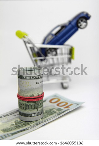 Car purchase.  Dollar banknotes,  toy blue car and shopping trolley . White background.