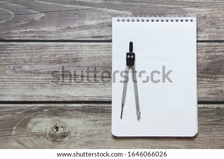 Notepad with a blank white sheet in a checker paper with compass lies on the background of wooden boards.