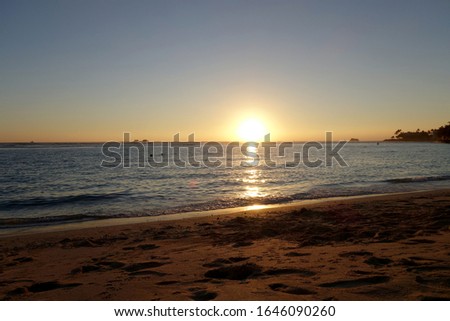 Sunset as wave lap towards the beach from the ocean at Ala Moana Beach Park on Oahu, Hawaii.