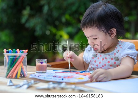 Cute little Asian girl in a white dress is drawing with painting fun