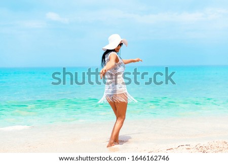 A woman with black hair in white dress dancing by the water on the beautiful turquoise beach