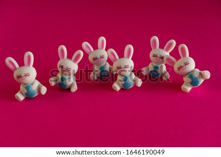 Smiling, dancing rabbit figurines with Easter eggs, fun, whimsical holiday art on bright pink background.